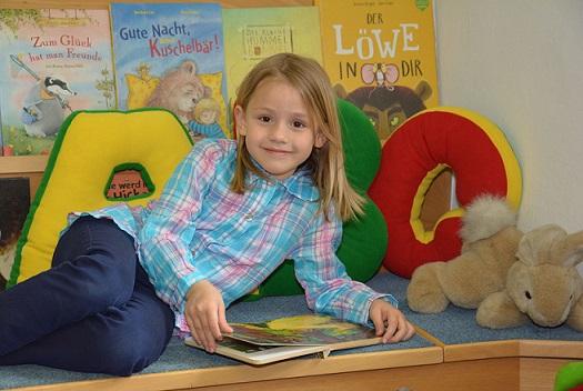 Bub am Unterarm abgestützt mit einem Buch vor sich im Kinderbereich